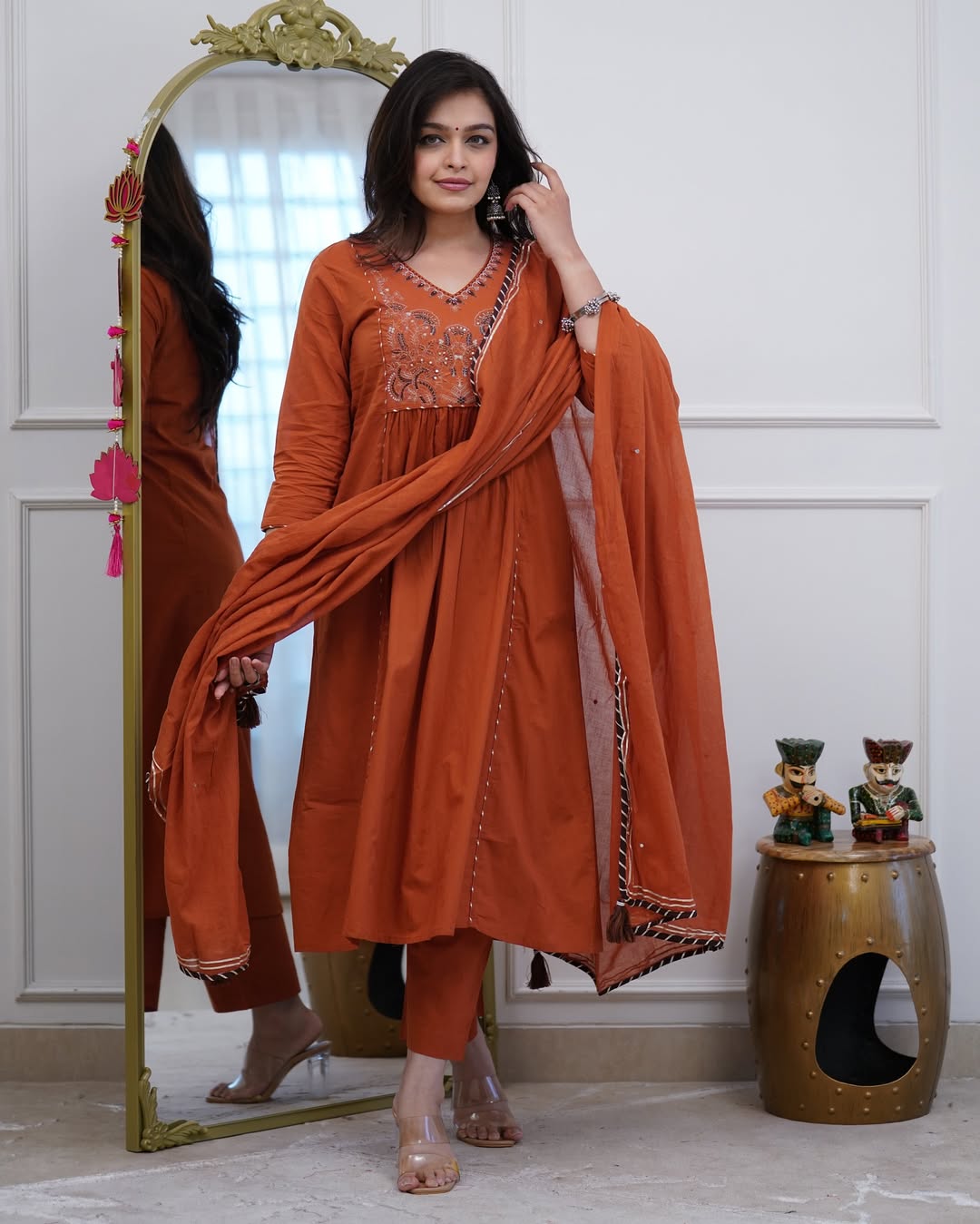 Woman in an orange traditional outfit standing in front of a mirror.